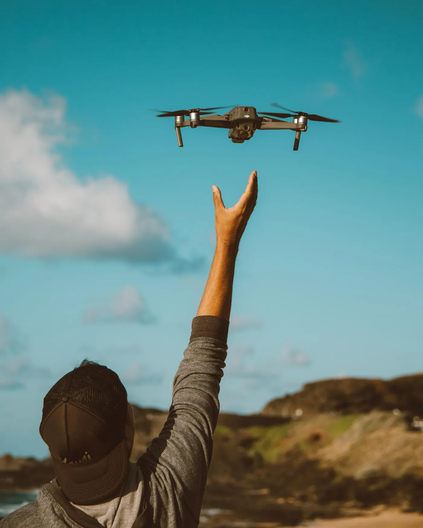 A drone pilot launching a camera drone under a clear sky